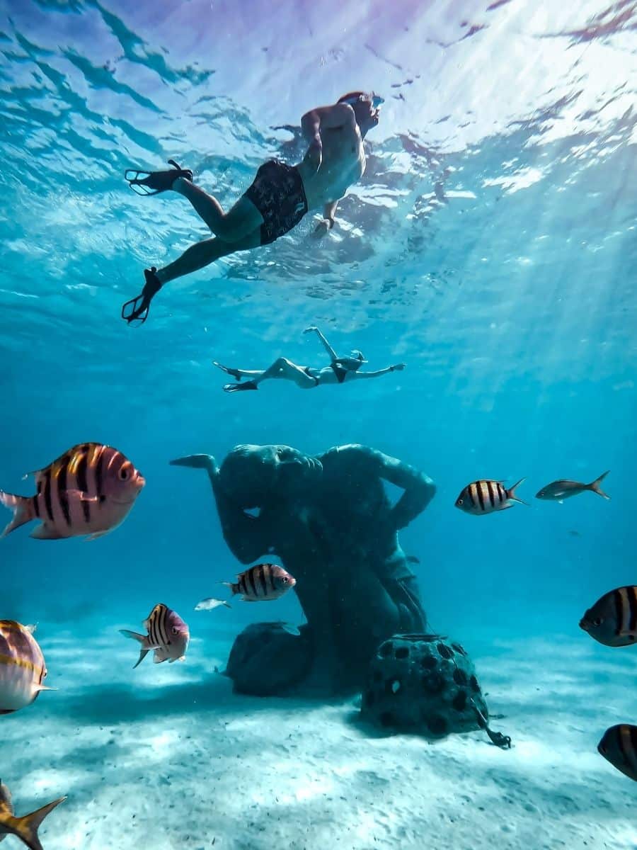 adventure couple snorkeling with underwater sculpture at clifton heritage national park in the carribean