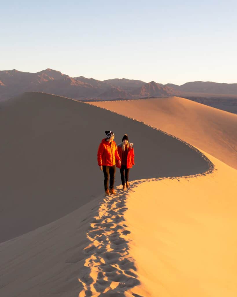 adventure couple hiking up mesquite flat sand dunes at sunrise in death valley