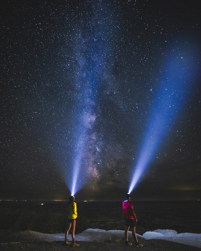 adventure couple admiring the Milky Way in Badlands National park at night time with headlamp beams at the stars