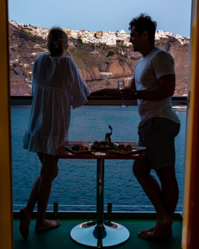 Adventure couple looking at Fira, Santorini cruise port from balcony stateroom on cruise ship