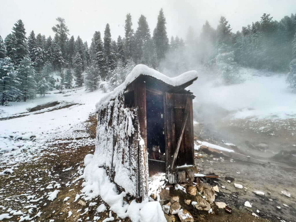 Woman sitting in outhouse with hot spring tub in Idaho