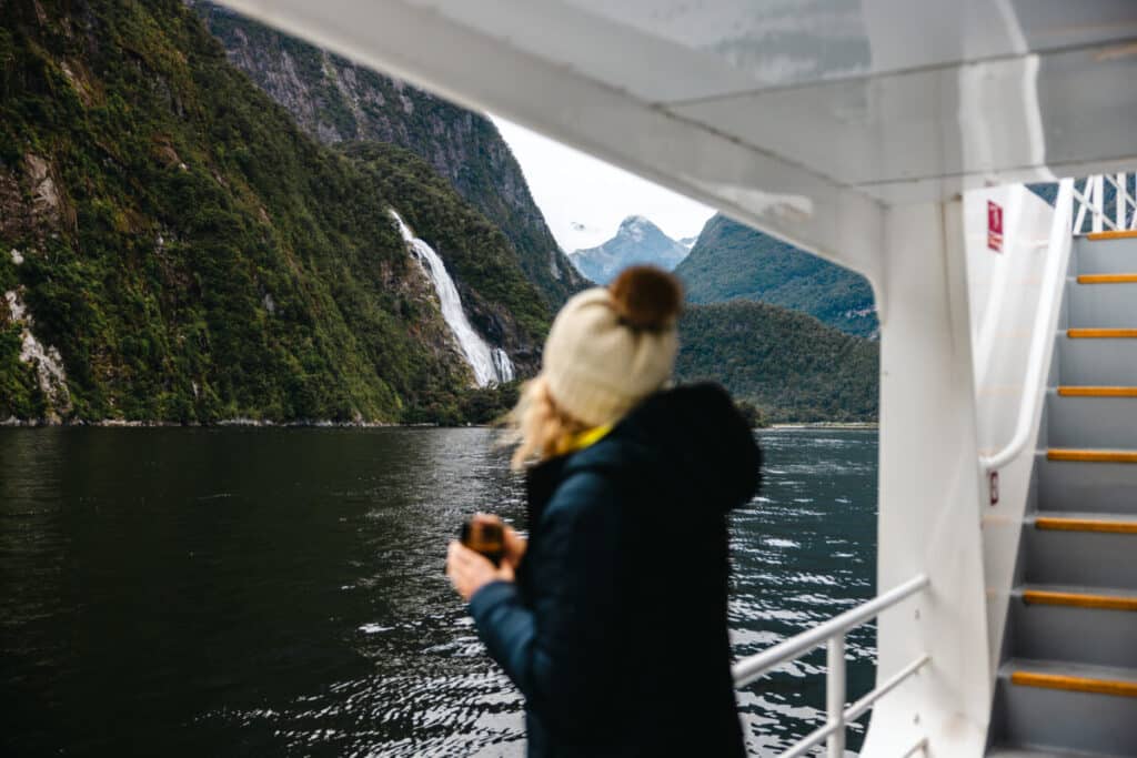 Woman drinking coffee in front of waterfall in Milford Sound New Zealand