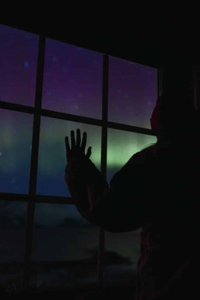 woman's silhoutette looking outside the window staring at the Northern Lights