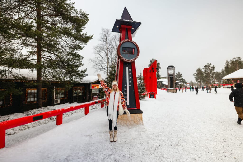 Woman standing in front of Arctic Circle sign at Santa Claus Village in Rovaniemi, Finland.