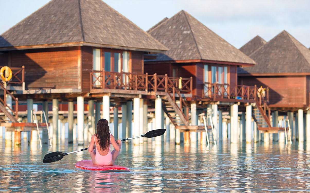 A Woman Paddleboarding Next to Overwater Bungalows