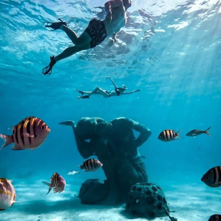 adventure couple snorkeling with underwater sculpture at clifton heritage national park in the carribean